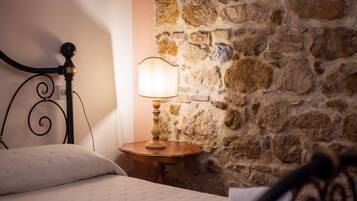 A bed with a headboard, a bedside lamp, and a stone wall.