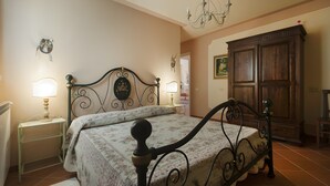 A bedroom with a bed, bedside lamps, a dresser, and a chandelier. - Agriturismo I Borghi – Apartment Liquirizia with Pool in San Gimignano (San Gimignano)