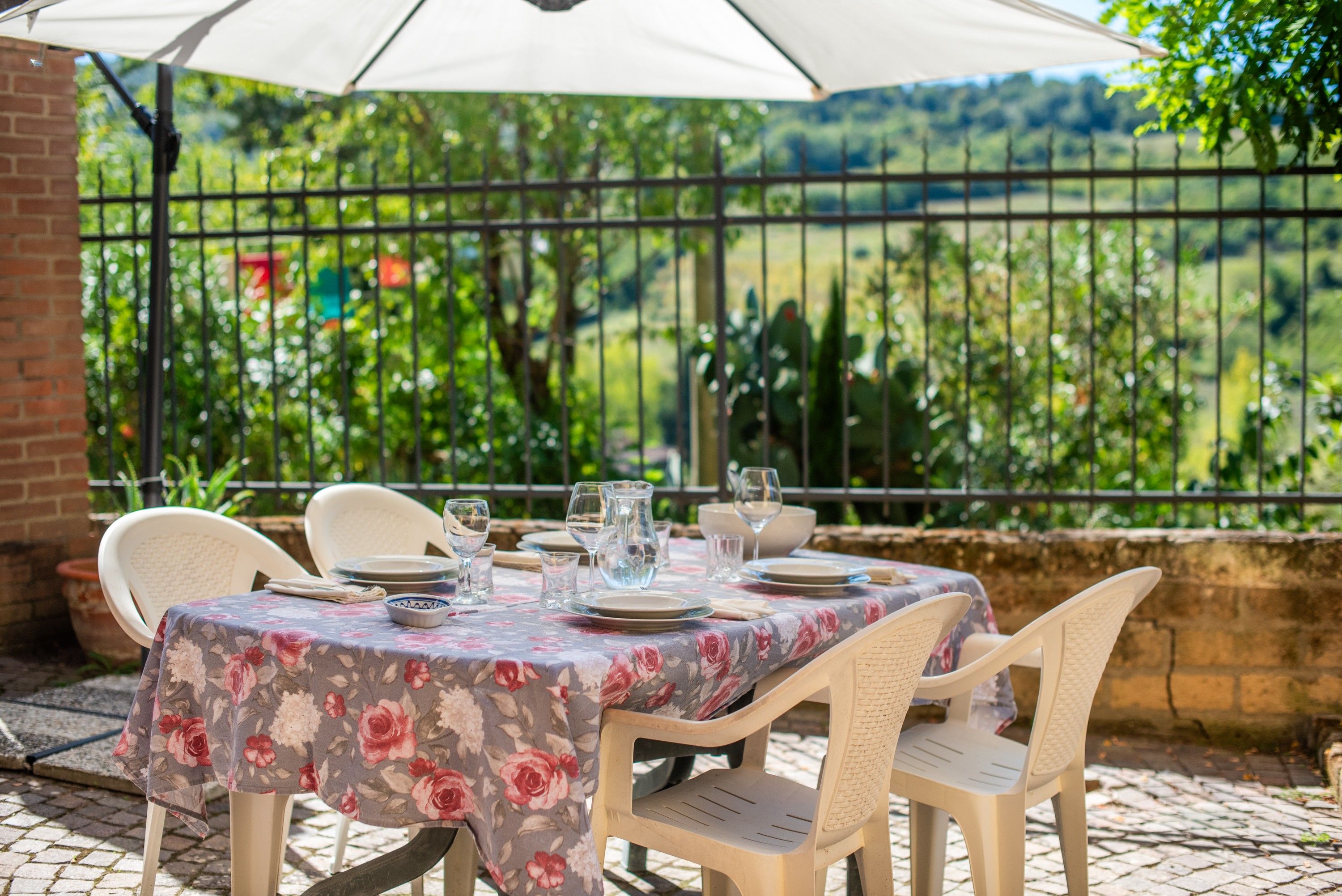 An outdoor dining area with a table set for four, surrounded by chairs, under a canopy.