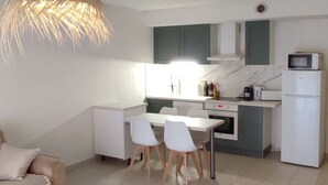 A modern kitchen with white cabinets, a dining table with chairs, and a hanging light fixture. - Relaxing vacations (Canet-en-Roussillon)