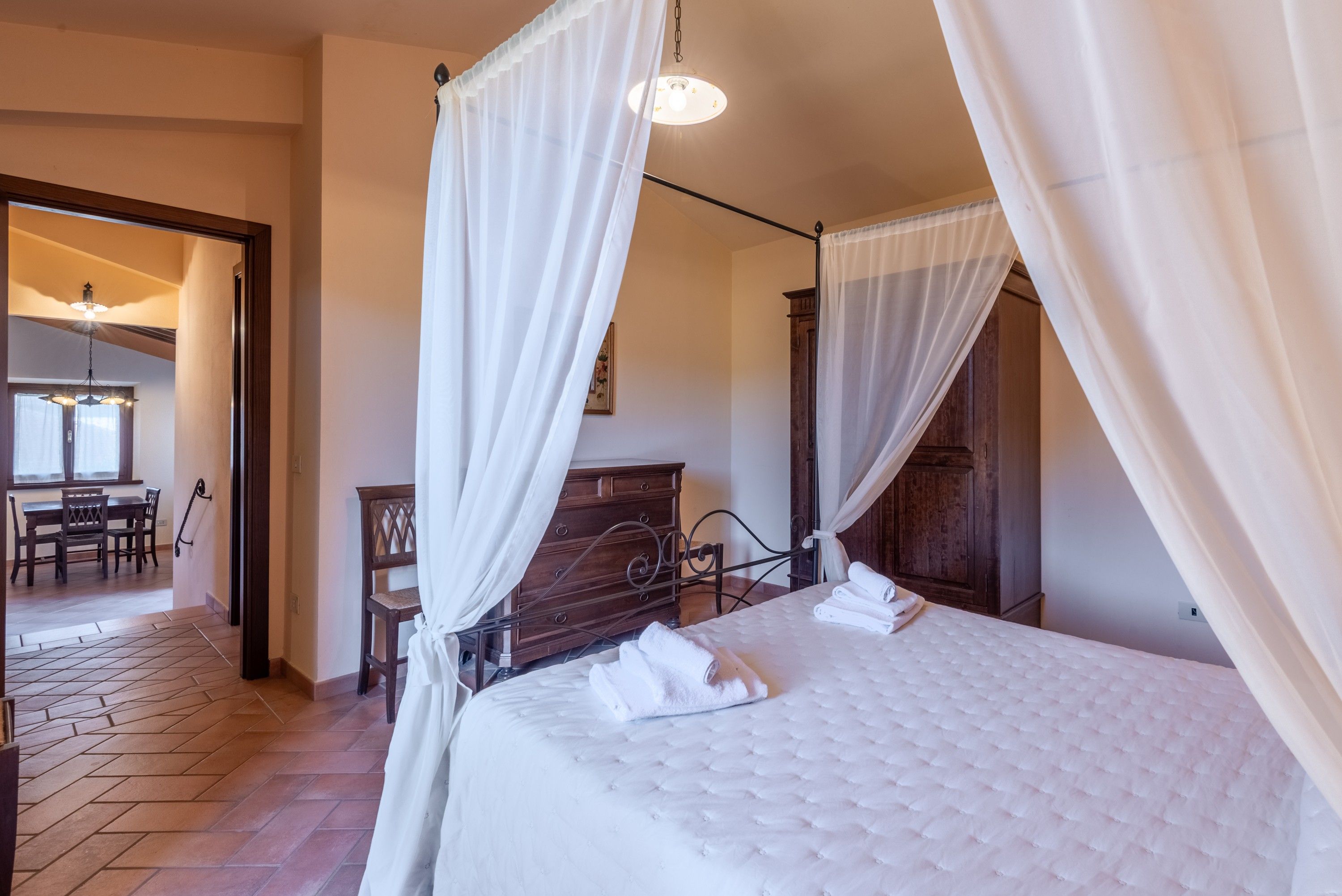 Ein Schlafzimmer mit einem Himmelbett, einem Holzkopfstück und einem großen Fenster mit Vorhängen.