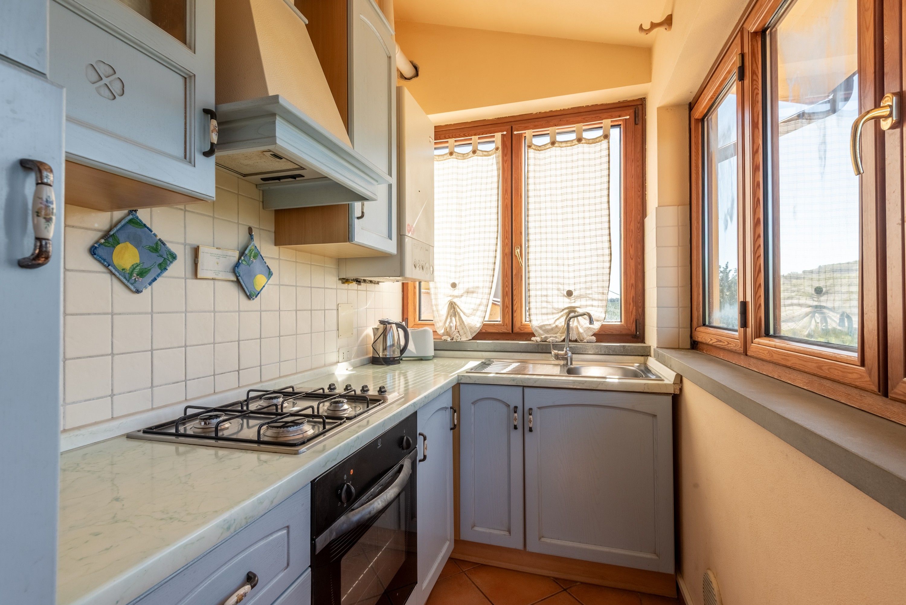 Una cucina con piano cottura a gas, forno e una finestra con tende.