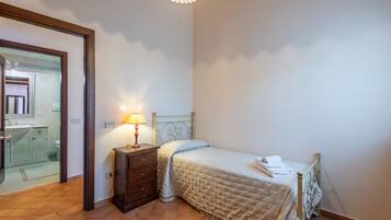 Ein Schlafzimmer mit Bett, Nachttisch, Lampe und einem durchgegangenen Türspalt sichtbaren Badezimmer.