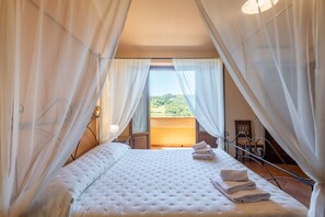 Un dormitorio con una cama grande, cortinas blancas y vistas a un paisaje verde.