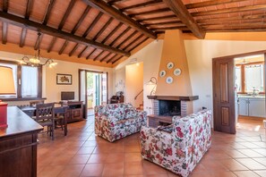 Un salón amplio con chimenea, vigas de madera y un comedor con televisor.