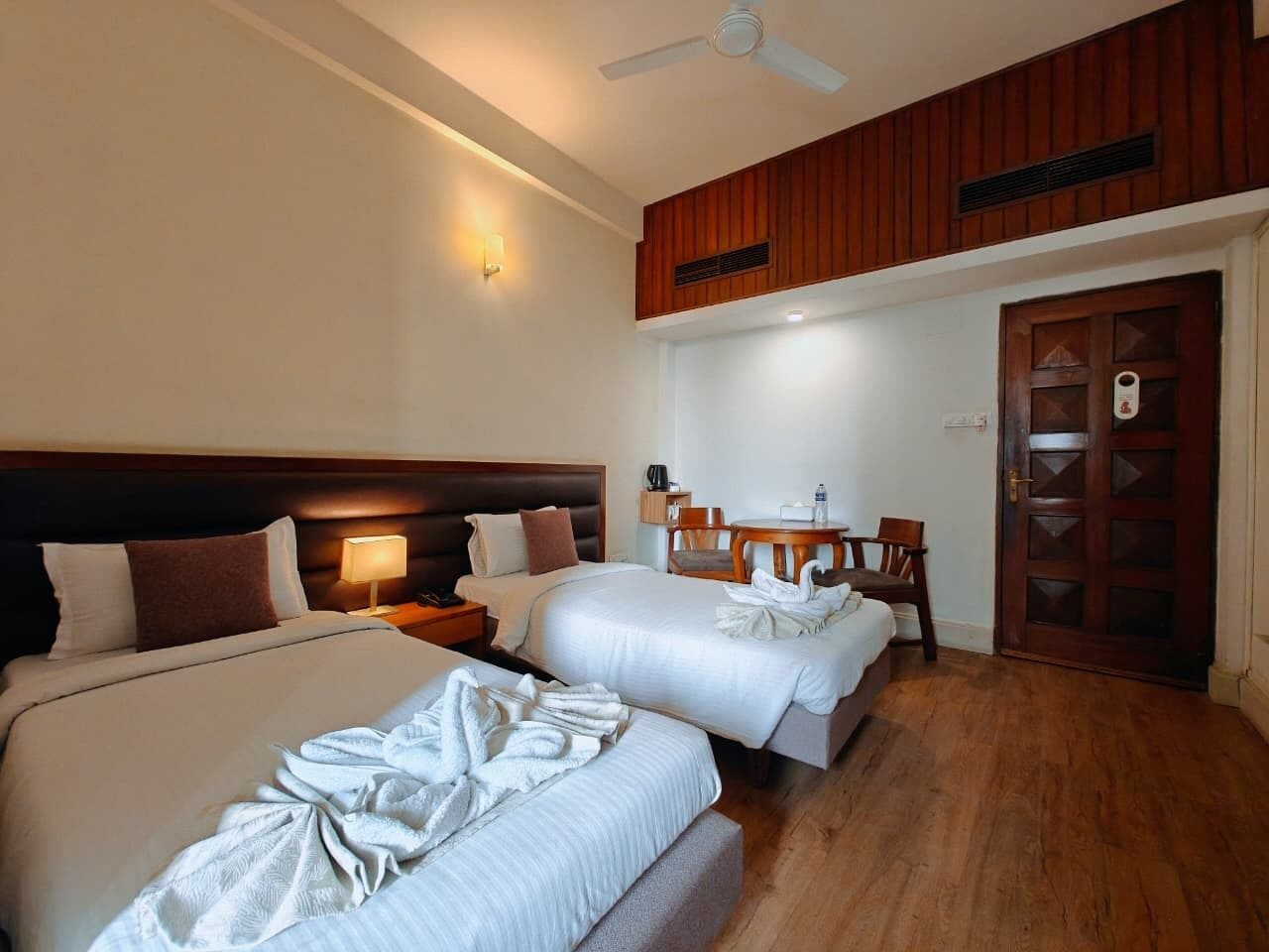 A hotel room with two beds, a desk, a chair, a wardrobe, and a ceiling fan.