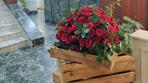 Un'area reception con una scrivania in legno, un quadro con un uccello e una cassa di legno piena di rose rosse.