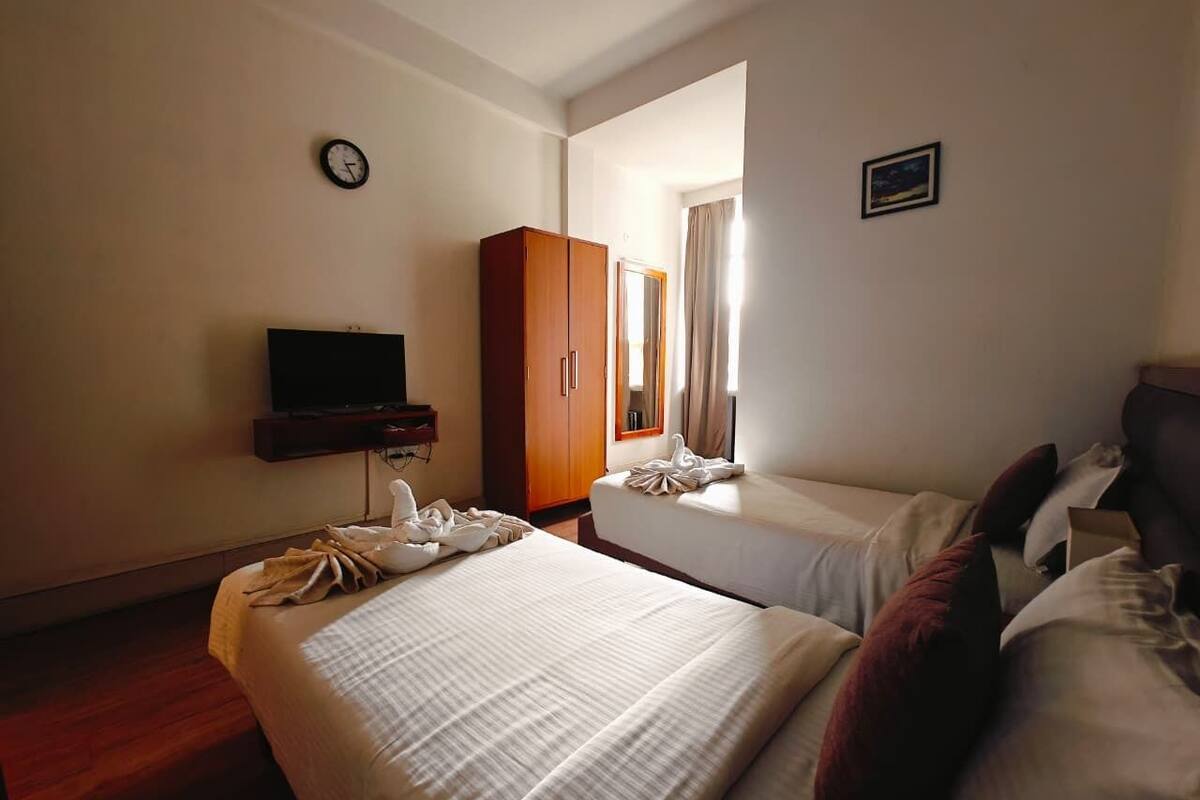 A hotel room with two beds, a wardrobe, a television, and a window with curtains.