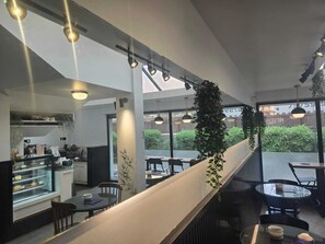 A modern restaurant with a long counter, hanging plants, and a view of the outside.