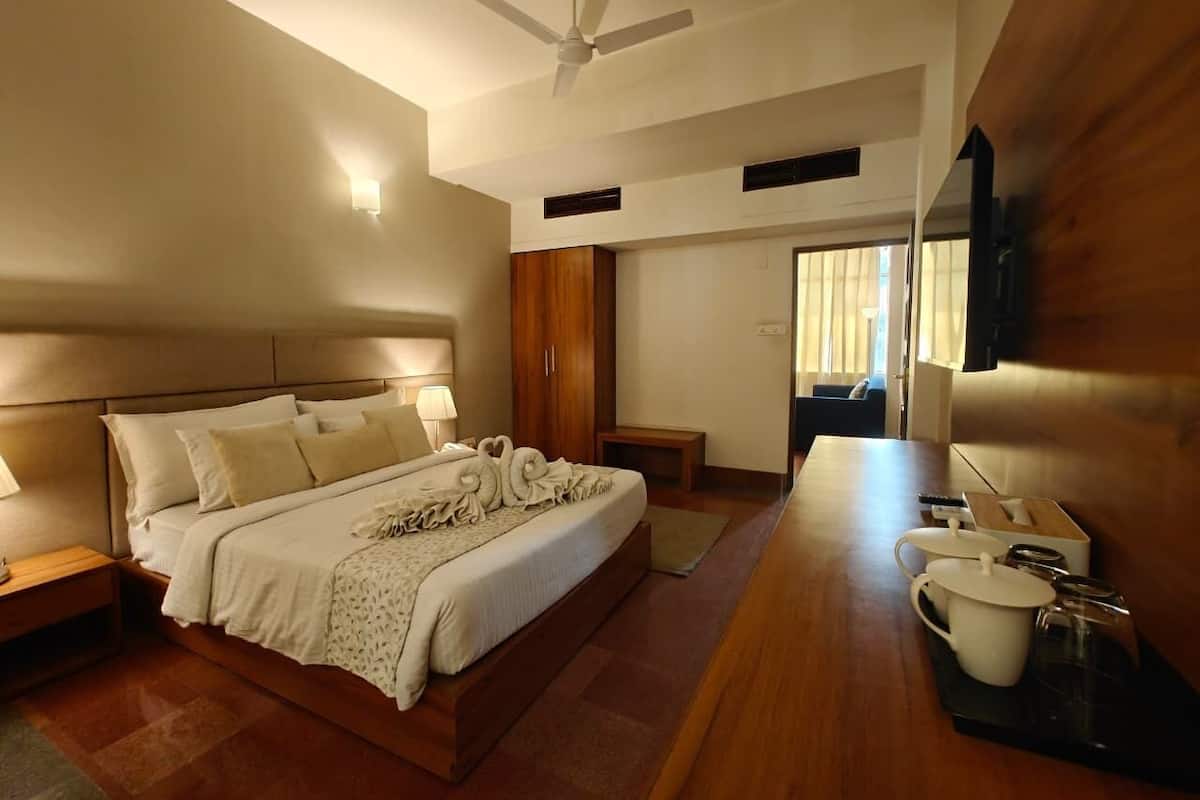 A hotel room with a large bed, bedside tables, a desk with a chair, a ceiling fan, and a large mirror.