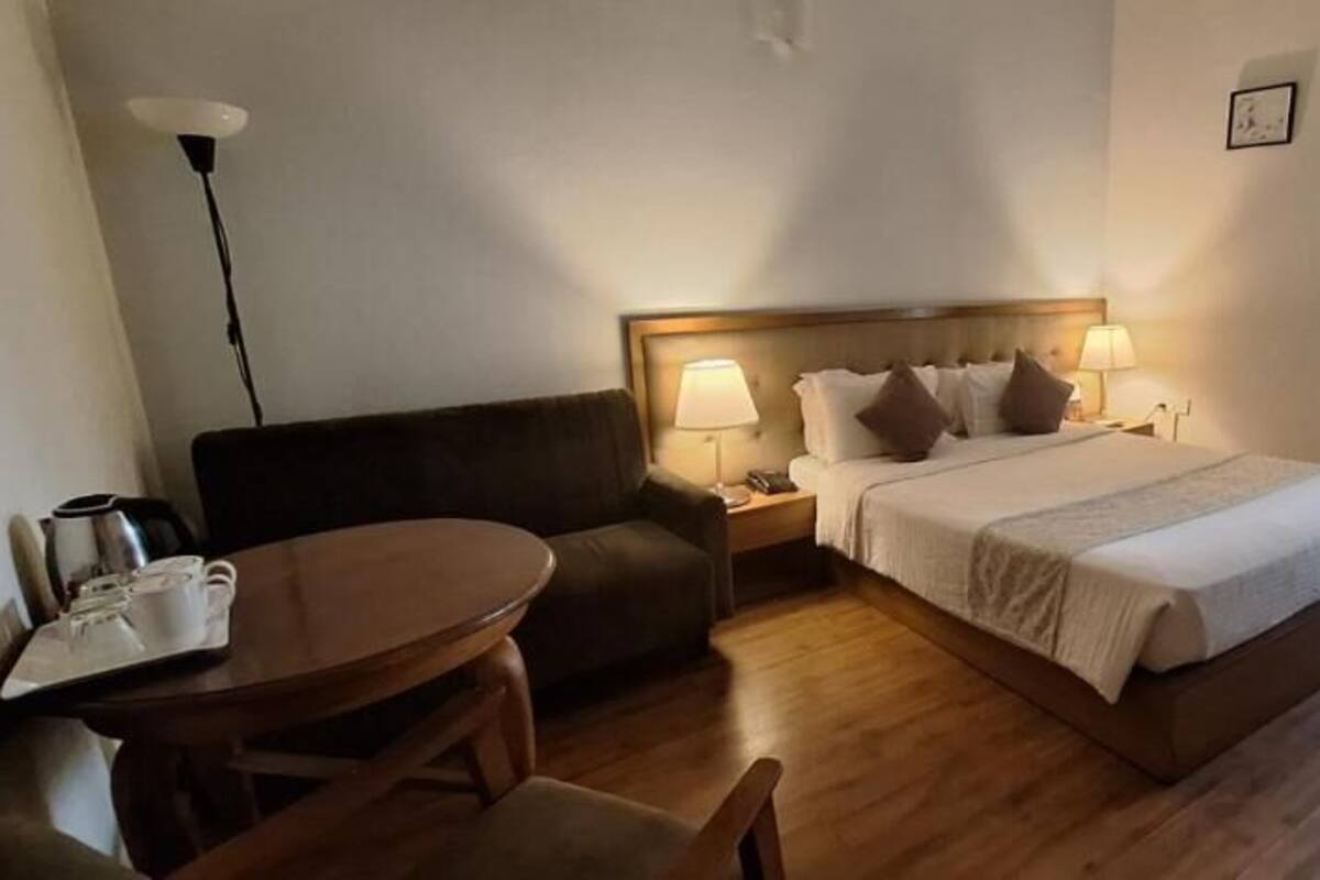 A hotel room with a bed, bedside lamps, a sofa, a table, and a coffee maker.