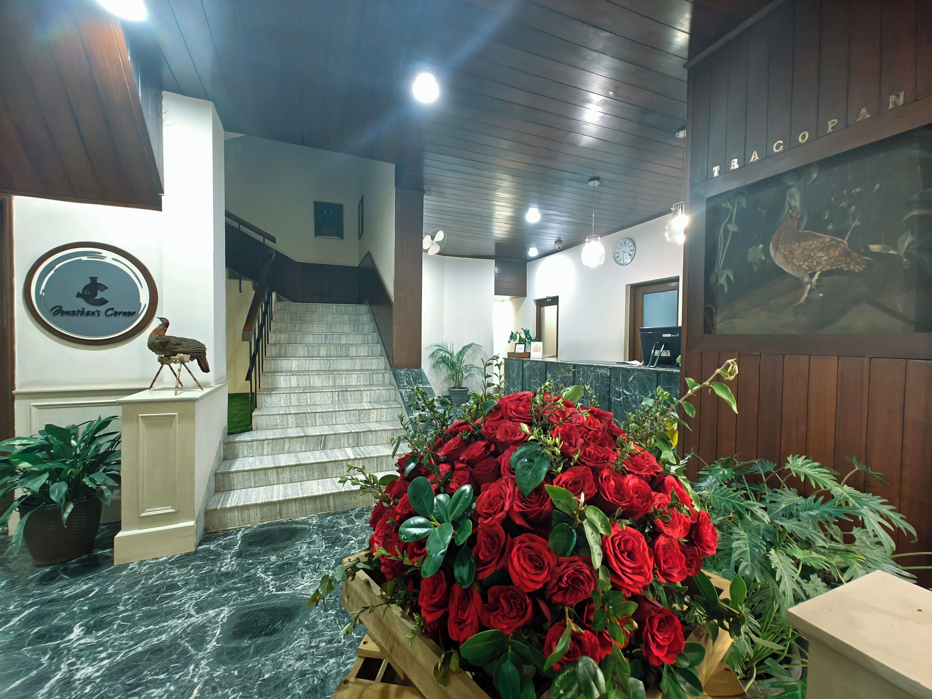 A reception area with a marble floor, a wooden staircase, a wall-mounted sign with a bird logo, and a large display of red roses.