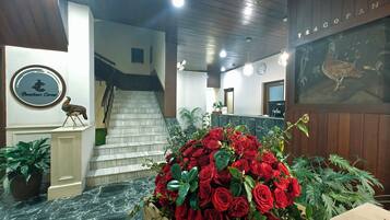 A reception area with a marble floor, a wooden staircase, a wall-mounted sign with a bird logo, and a large display of red roses.