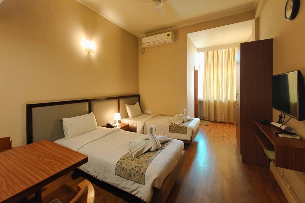 A hotel room with two beds, a wooden desk, a TV, and an air conditioning unit.