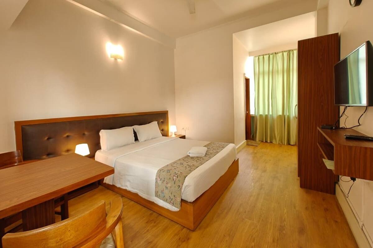A hotel room with a bed, a desk, a chair, a television, and a ceiling fan.