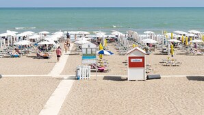 Une plage dotée de nombreuses chaises longues et de parasols, d’une tour de surveillance pour les sauveteurs, et d’un panneau indiquant l’emplacement d’un bar.