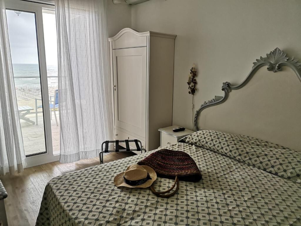 Een slaapkamer met een bed, een kledingkast, een nachtkastje en uitzicht op het strand.