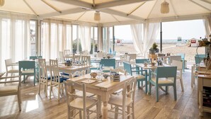 Un restaurant situé en bord de mer, doté de nombreuses tables et chaises, de grandes fenêtres et offrant une vue sur la plage.
