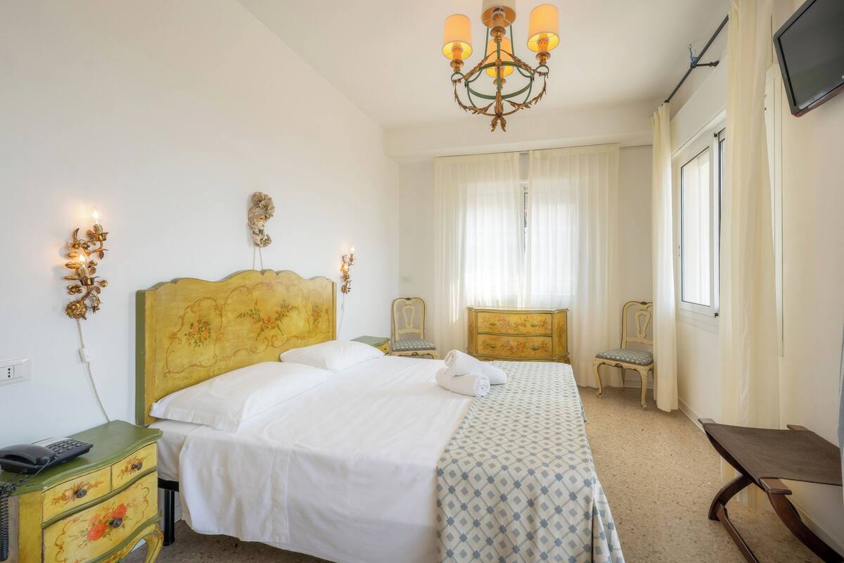 Een hotelkamer met een bed, bureau, stoel, televisie en een kroonluchter.