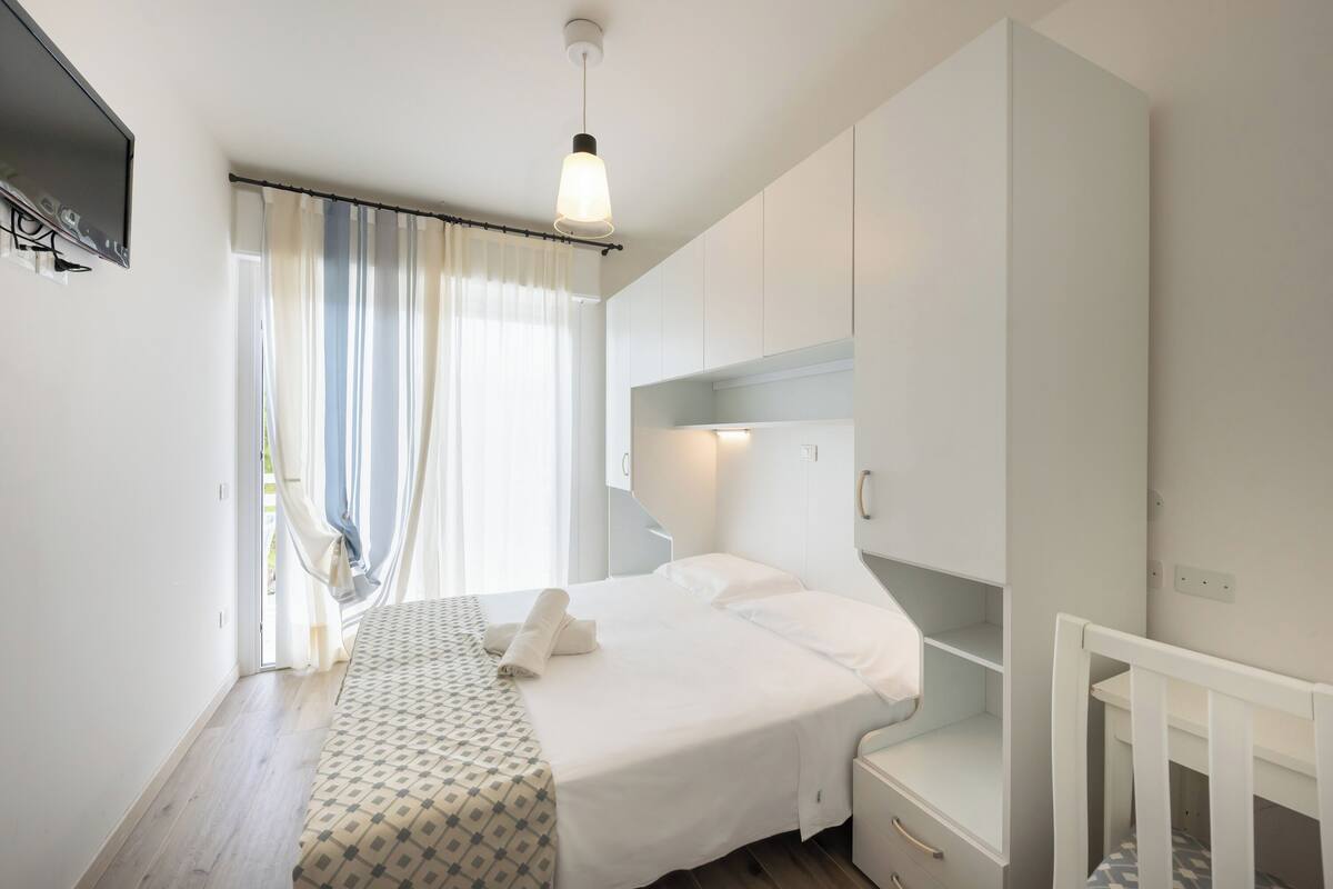 Een slaapkamer met een bed, een babybedje, een televisie en een raam met gordijnen.