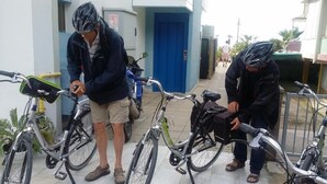 L’entrée d’un immeuble avec une porte bleue, un vélo garé devant et une personne qui ajuste un vélo.