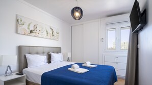 Una camera d'albergo con un letto, un comodino, una TV a schermo piatto e una finestra con tende.