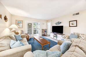Ein Wohnzimmer mit beigefarbenen Sofas, einem Couchtisch, einem Fernseher und einem Bücherregal.