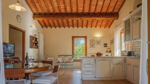 Een ruime keuken met houten vloeren, een eethoek met een tafel en stoelen, en een groot raam dat zorgt voor veel daglicht.
