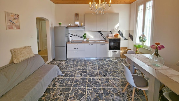 Una cocina moderna con encimeras de mármol, una araña y un comedor con mesa y sillas.