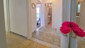 Un pasillo con suelo de baldosas, techo de madera y un espejo que refleja un baño.