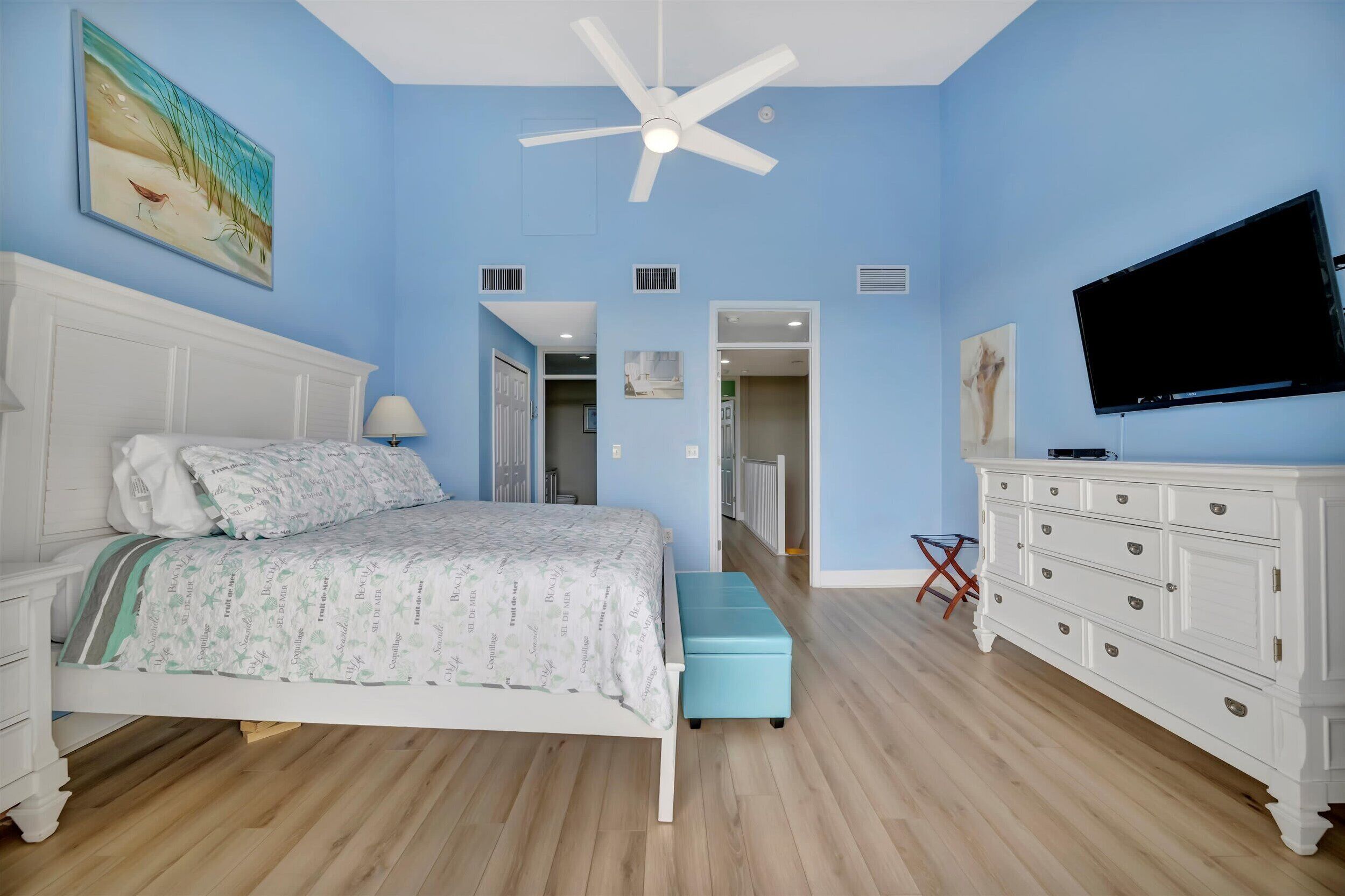 A bedroom with a bed, a dresser, a television, and a ceiling fan.