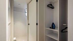 A modern bathroom with white tiles, a shower area, and a walk-in closet with shelves and hangers. - w Amazing 2BR in Roma Norte (Mexico City)