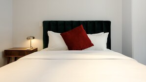 A neatly made bed with white and red pillows, a dark headboard, and a small bedside table with a lamp. - w Amazing 2BR in Roma Norte (Mexico City)