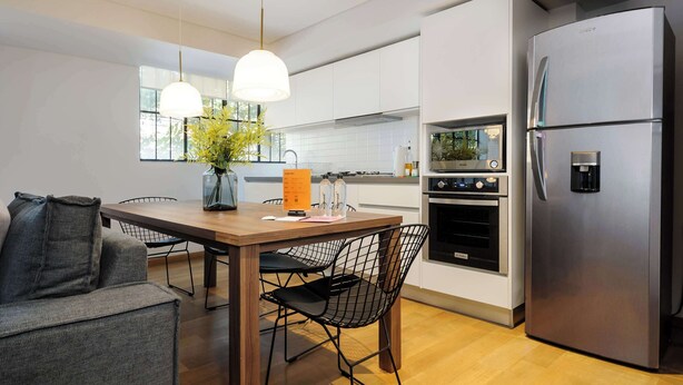 A modern kitchen with a stainless steel refrigerator, wooden dining table, and black wire chairs. - w Amazing 2BR in Roma Norte (Mexico City)