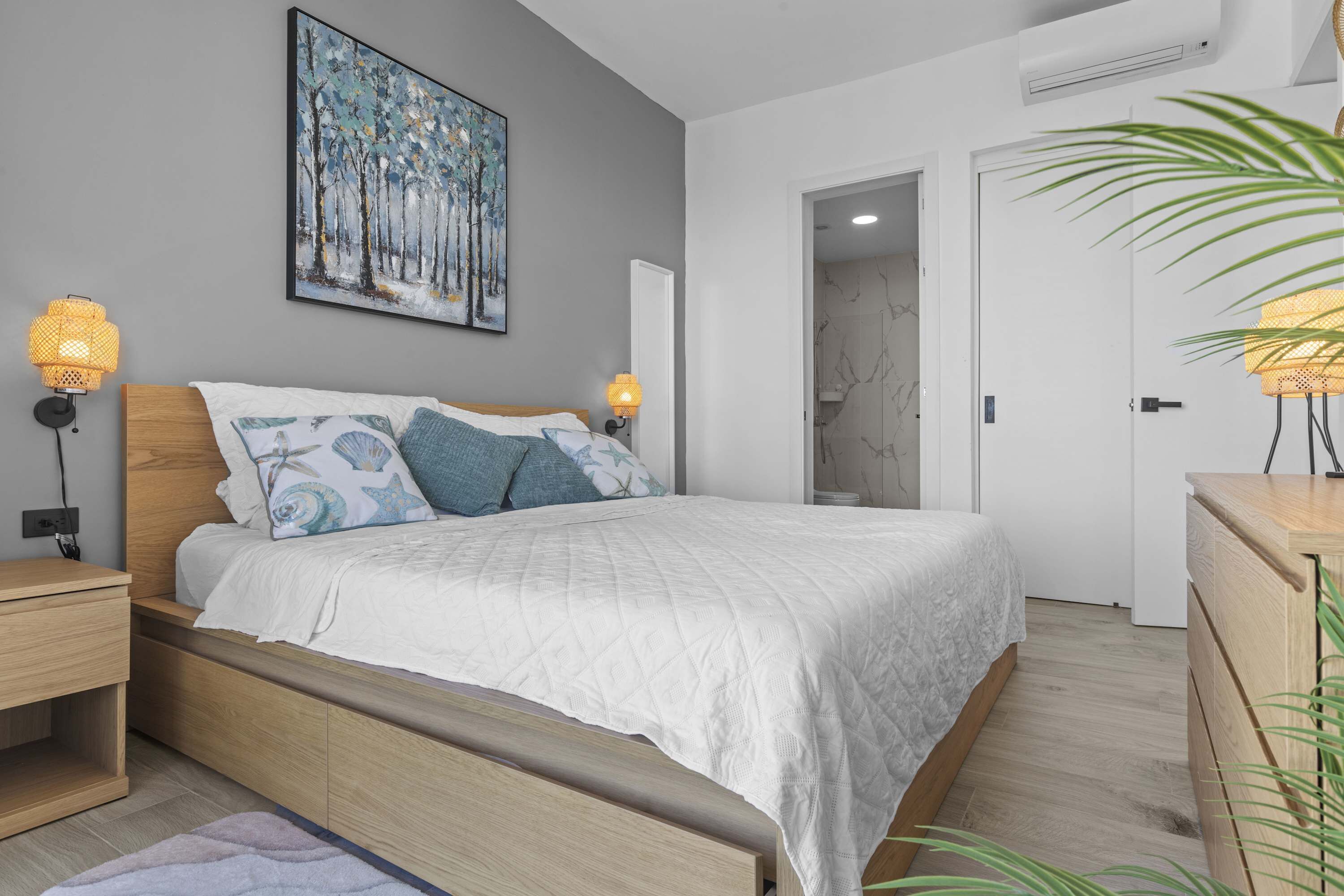 Une chambre à coucher comprenant un lit, des lampes de chevet, une table de nuit, une tête de lit en bois, un tableau accroché au mur et une porte donnant sur une autre pièce.