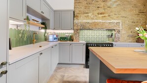Une cuisine avec des meubles de couleur gris clair, un plan de travail en bois, un four encastré et un mur en pierre.