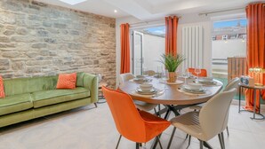 Un coin repas avec un mur en pierre, un canapé vert, des chaises orange et une table dressée pour quatre personnes.