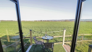 Een balkon met een tafel en stoelen, met uitzicht op een groen veld.
