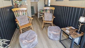 Een gezellige kamer met twee houten schommelstoelen, een kleine tafel met een lamp, en een trap naar een andere kamer.