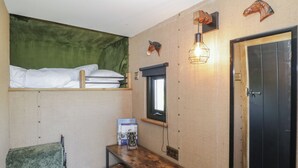 Een compacte kamer met een stapelbed, een klein tafeltje met manden, een spiegel aan de muur en een deur met een greep.