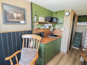 A compact kitchen with a wooden chair, a sink, and a clock on the wall.