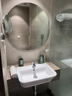 Un baño moderno con un lavamanos blanco, un espejo redondo y una cabina de ducha de vidrio.