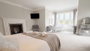 A bedroom with a large bed, a fireplace, a bathtub, and a large window with curtains. - Hanlith Hall (Skipton)
