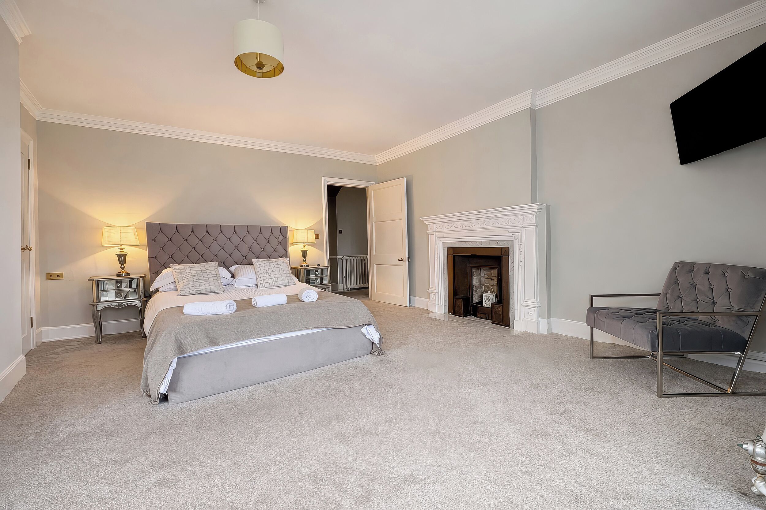 A bedroom with a large bed, a fireplace, a TV mounted on the wall, and a chair.