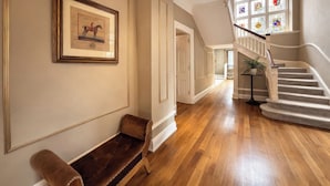 A hallway with a wooden bench, framed artwork, a staircase with a railing, and a stained glass window. - Hanlith Hall (Skipton)