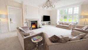 A spacious living room with a fireplace, sofas, a television, and large windows. - Hanlith Hall (Skipton)