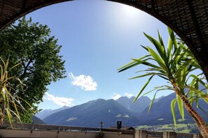 A view through a circular window overlooking a mountainous landscape with greenery and a clear sky.