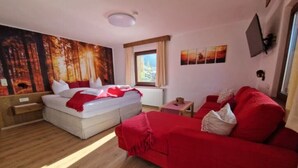 Un dormitorio con cama, sofá rojo, ventana y un cuadro en la pared.