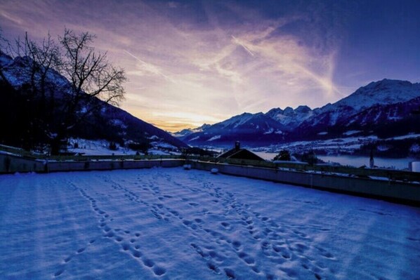 A snowy landscape with mountains, a clear sky, and footprints in the snow.