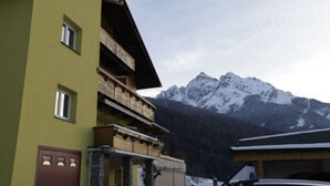 Un edificio de varios pisos con balcones, un garaje y montañas al fondo.